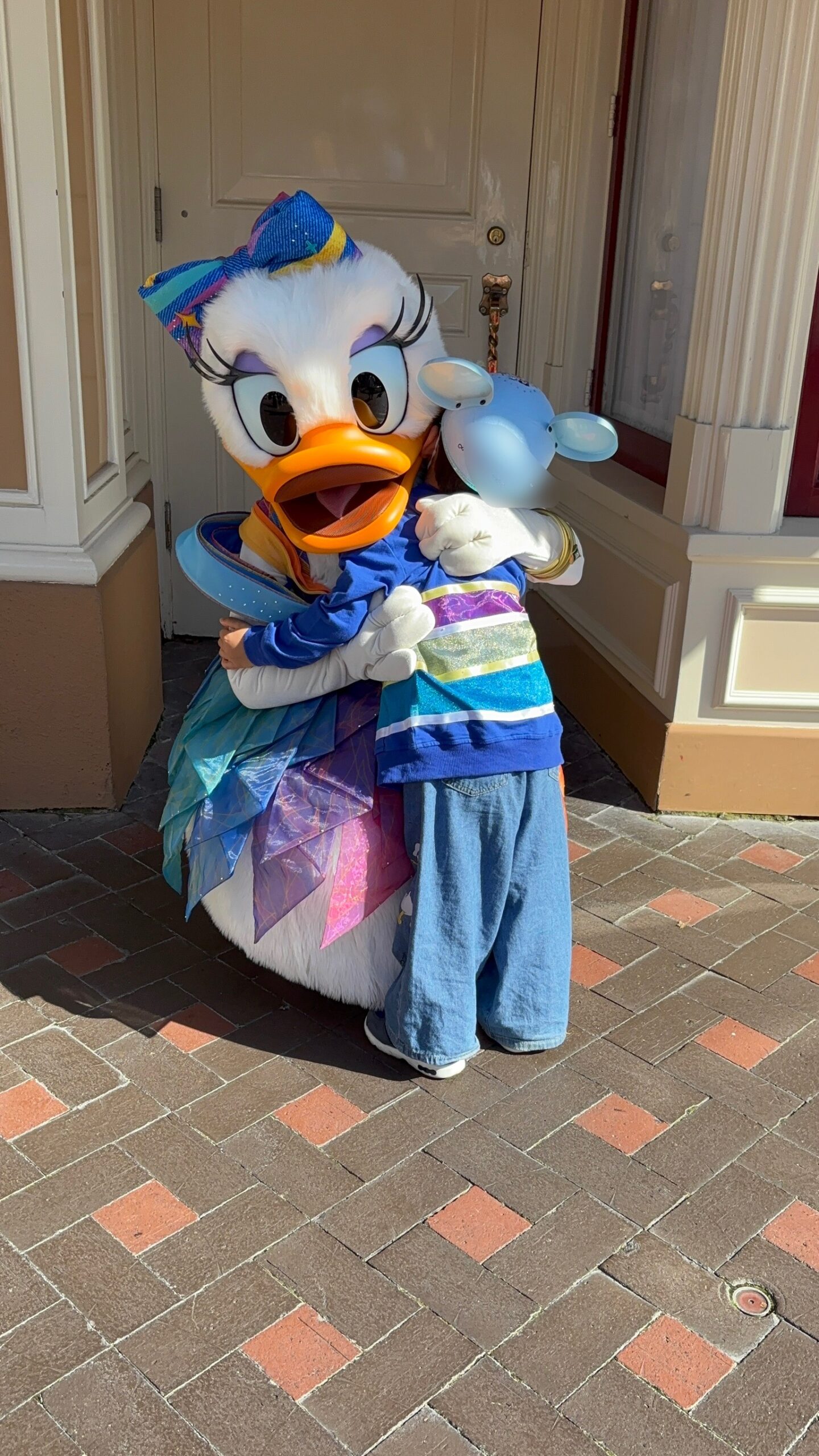 アナハイムディズニー70周年アウトフィットのデイジーが息子を優しくハグしているグリーティング写真。