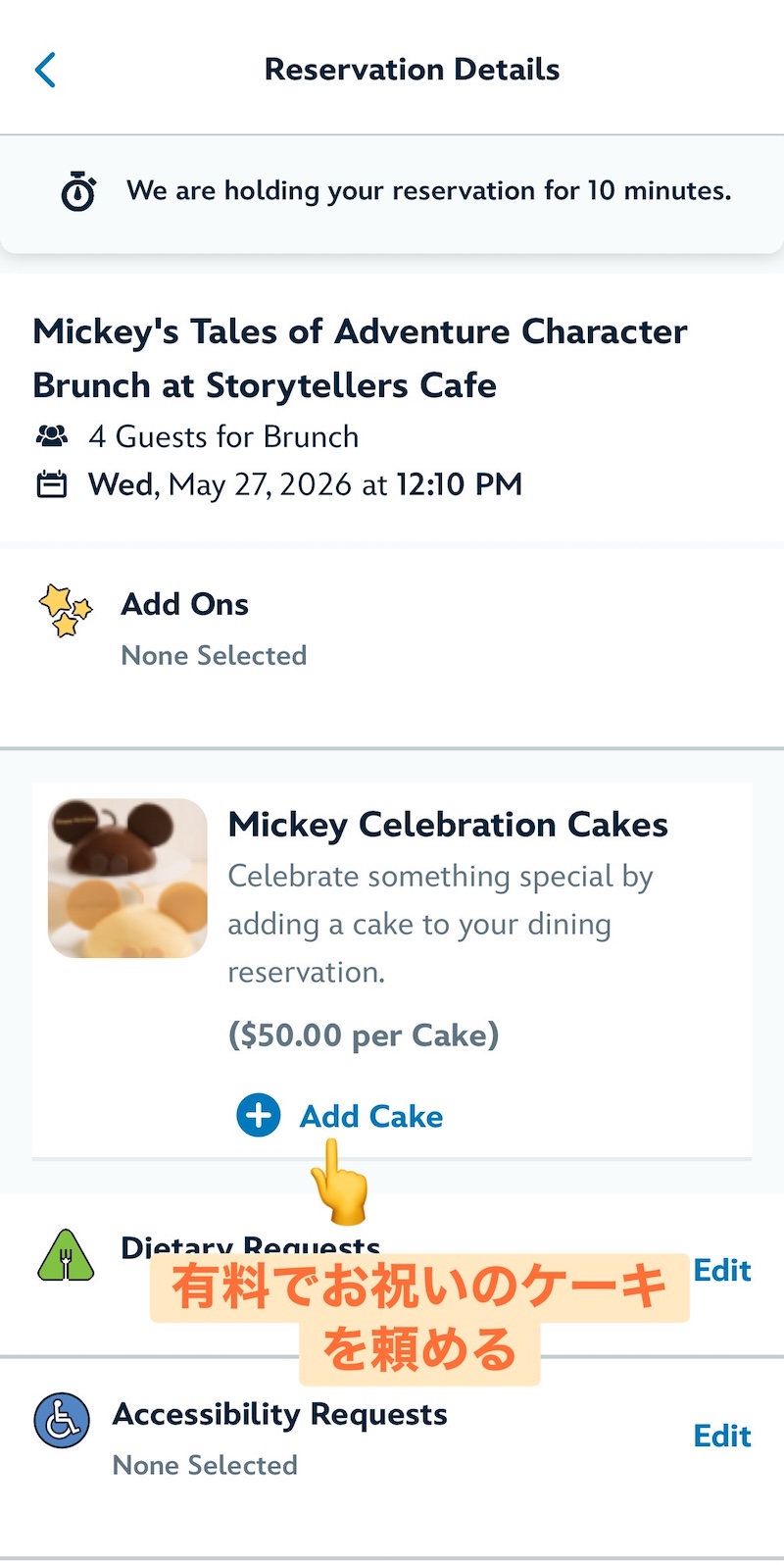 ディズニーランド公式アプリのストーリーテラーズカフェ予約画面で27日12時10分を選択した状態のスクリーンショット。お祝いケーキの追加オプションに指マークで印がついている