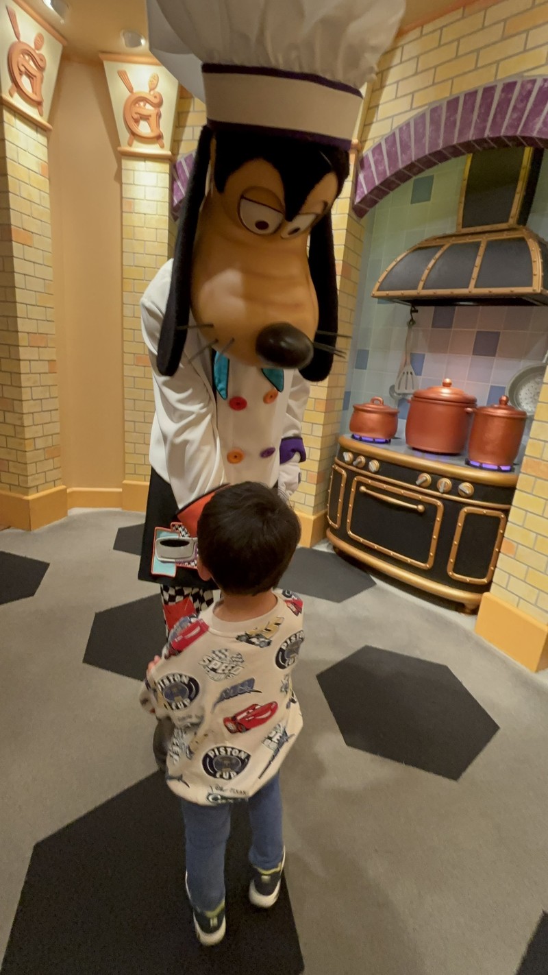 グーフィーズキッチンのフォトブースで息子とグーフィーが握手している写真。コンロにかかったお鍋に火がついている様子がよくわかる