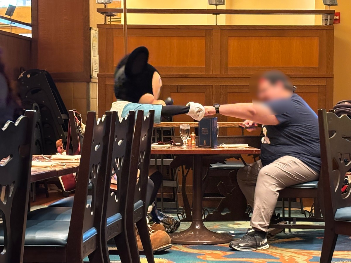 ストーリーテラーズカフェで他のゲストのテーブルの空いている席に座ってタッチをしているミッキーマウスの写真